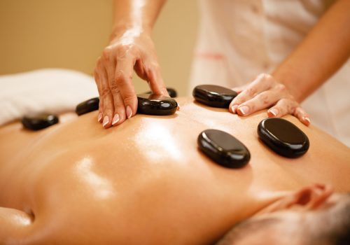 Close-up of therapists placing hot stones on man's back during lastone therapy at the spa.